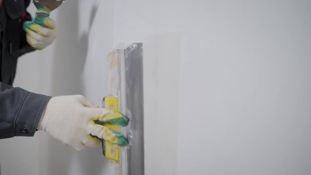 a close shot at the builder hands, who level the wall with a long spatula and plaster, the man applies the composition on the surface