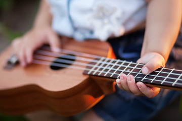 Little girl playing ukulele outdoors.