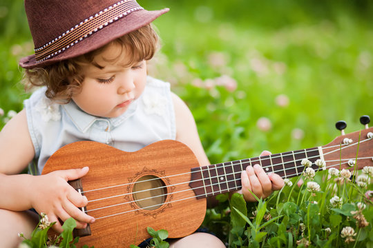 Little girl playing ukulele outdoors.