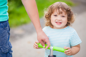 Father teaching his adorable toddler daughter to ride kick scoot.