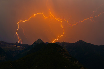 spectacular double lightning bolt strike in mountain peak silhouette, orange sky