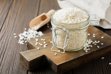 Raw  White rice variety Arborio for Italian risotto dishes in glass jar on  dark wooden background. Selective focus. Copy space.