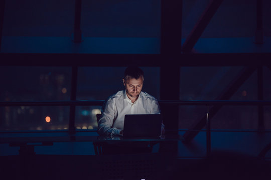 Businessman working on laptop in night office.