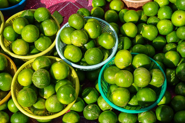 Baskets of fresh rounded organic lime fruit background in bright yellow and green color selling in market under sunlight with light reflection skin and shadow
