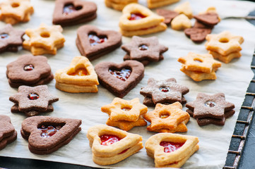 Different shapes of festive cookies with jam on a baking paper.
