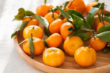 Plate of fresh and juicy tangerines with leaves on a white stone background. Close up and copy space.