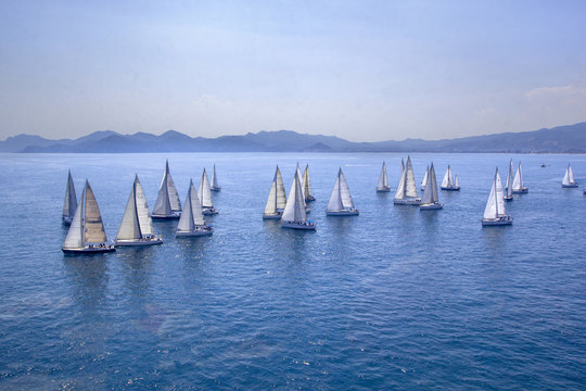 Sailing regatta or a group of small water racing boats in the Mediterranean, a panoramic view with blue mountains on a horizon