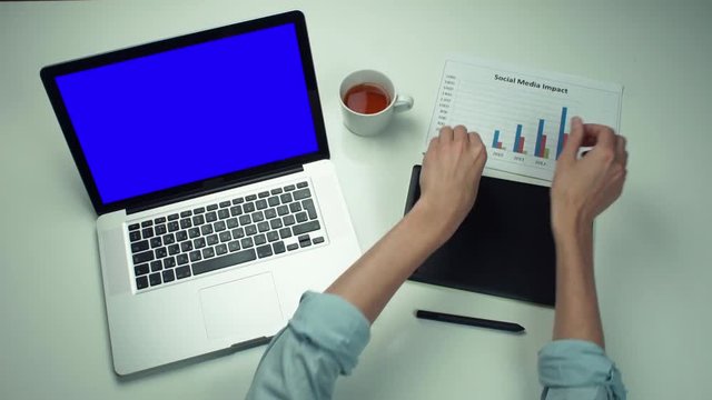 Top view male hands working with printed graphs using laptop with green screen