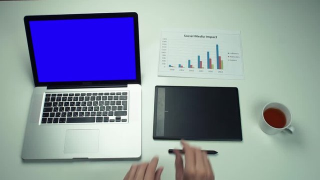 Top view male hands working with printed graphs using laptop with green screen