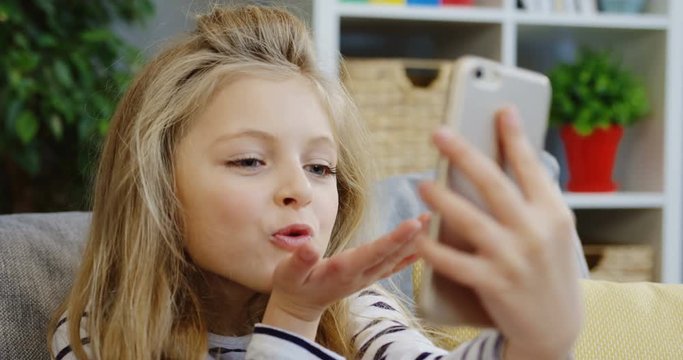 Close up of the cute blonde little girl making selfies on the smartphone in the living room. At home. Portrait. Inside