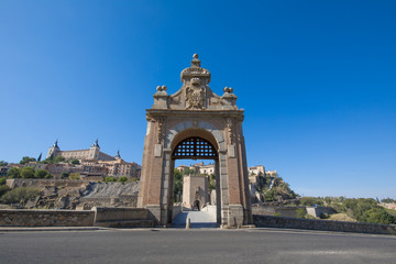 first door of Alcantara bridge, landmark and monument from ancient Roman age, with Alcazar and Toledo city in background, Spain, Europe
