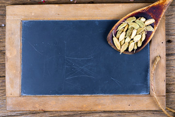 Ein alter Holzlöffel mit ganzen Kardamomkapseln liegt auf einer alten Schiefertafel mit...