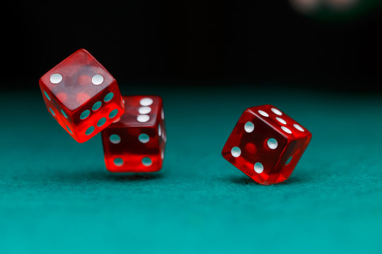 Image of several red dice falling on green table on black background