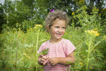 In summer in the meadow a small happy girl stands in yellow flowers.