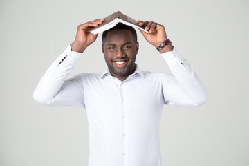 Business man holds an open book in the form of a roof over his head. Attractive handsome happy smiling afro american male.