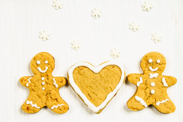 Gingerbread men friends near the heart on a white wooden table.