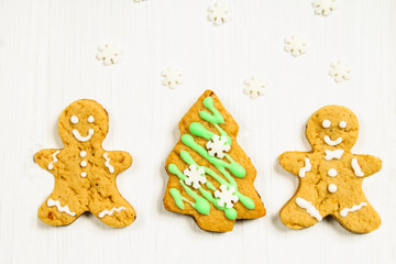 Gingerbread men friends at the Christmas tree on a white wooden table.