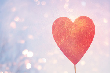 A man holds a red wooden heart on a stick against the background of nature, sky, stones. The concept of Valentine's Day.