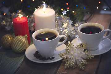 A romantic festive still life with burning candles, golden Christmas-tree decorations and two cups of freshly brewed coffee in a close up. Dark Christmas background. Blurred bokeh