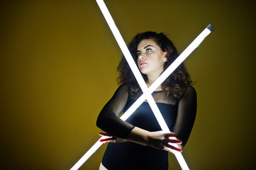 Curly brunette plus size model with two long led lamp against yellow wall.