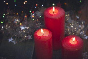 A romantic festive still life with red burning candles of different size. White and red colors. Blurred pine tree on the back. Blurred bokeh