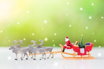 Miniature Santa Claus drive a wagon with a reindeer during the snowfall. Using as concept in Christmas day.