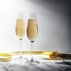 Two flute glasses with champagne on marble background. Direct light with heavy shadows. Square composition