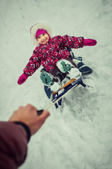 Fototapeta na wymiar young parent rolling little daughter in pink pattern coat on sled, smiling and having fun in the winter park. Concept of happy family