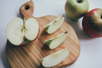 Healthy food - wood board with cut organic raw fruits on wooden background. Top view of sliced ingredients for fruit salad or snack - apple, pear, nuts, persimmon.