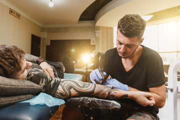 Professional tattooer artist doing picture on hand of man by machine black ink from a jar. Tattoo...