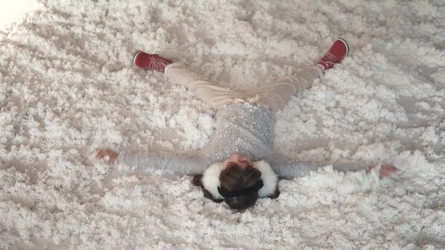 Christmas or New Year. child is making an angel lying on the snow. little girl fools around and lies in artificial snow. portrait of a child in Christmas decorations. slow motion