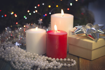 Obraz na płótnie Canvas A festive still life with a red and two white candles of different size, a beige gift box with a silver bow and white pearl beads. Dark Christmas background. Blurred bokeh