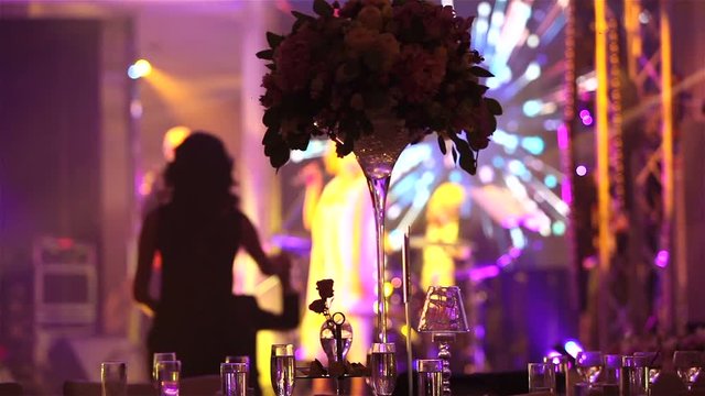 Group of silhouetted people dancing in a dark banquet hall for a wedding reception.The Wedding Banquet, people dance - shot through the wedding table decorations, wedding decoration
