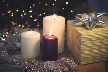 Obraz na płótnie Canvas A romantic festive still life with a purple and two white candles of different size, a beige striped gift box with a silver shiny and a light lilac garland of a ribbon and beads. Dark Christmas