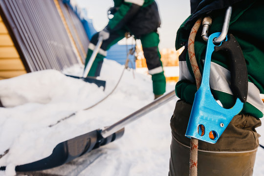 Carabiner For Installation Insurance, In Background Cleaning Roofs Of Buildings From Snow, Ice In Winter With Shovel.