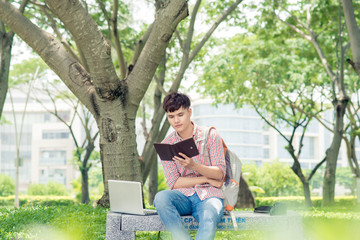 Young asian man with backpack reading a book