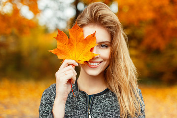 Beautiful happy woman with a smile holds an autumn yellow leaf near the face
