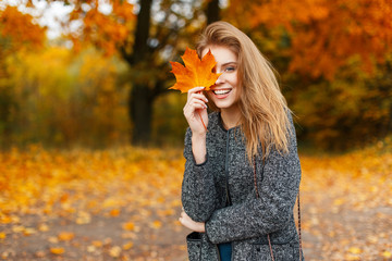 Happy young beautiful woman with a smile holds an autumn yellow leaf in the autumn day in the park