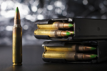 Five five six ammo with green tipped bullets stuffed into high capacity magazines with a silver bokeh background - obrazy, fototapety, plakaty