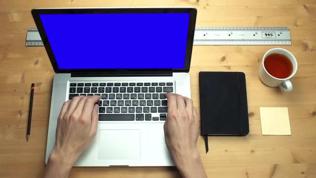Male hands using laptop with green screen at wooden desk. Office supplies