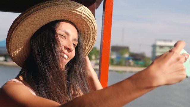Attractive Tourist Girl in Big Hat Taking Selfie Photo Using Mobile Phone and Cruise on Boat at River in Thailand. 4K Slow Motion.