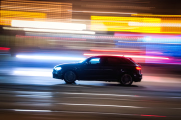 Plakat Automobile che sfreccia veloce di notte per le vie con luci colorate di una grande città 
