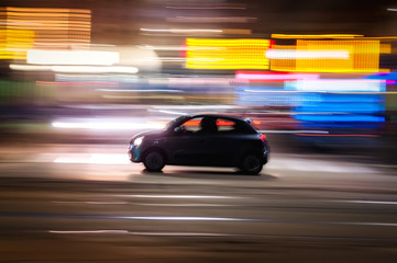 Fototapeta na wymiar Automobile che sfreccia veloce di notte per le vie con luci colorate di una grande città 