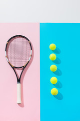 top view of tennis racket on pink and yellow balls in row on blue