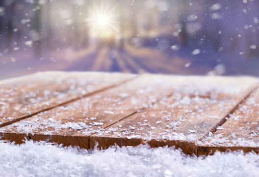 Wooden table top covered in snow with a Christmass, winter and snowy background with space to add products and text.