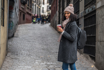 Naklejka premium Young black woman drinking coffee wandering in the streets of Madrid on winter