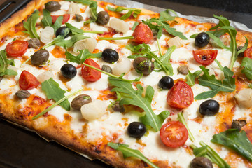 Pizza vegetariana con mozzarella, sugo, pomodorini, rucola, cipolle, olive, capperi e origano