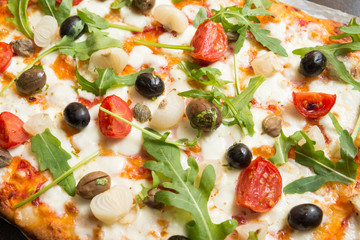 Pizza vegetariana con mozzarella, sugo, pomodorini, rucola, cipolle, olive, capperi e origano