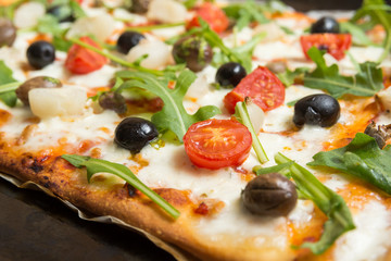 Pizza vegetariana con mozzarella, sugo, pomodorini, rucola, cipolle, olive, capperi e origano