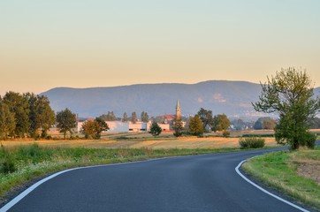 Summer rural landscape. Asphalt road with mountains and village in the background.